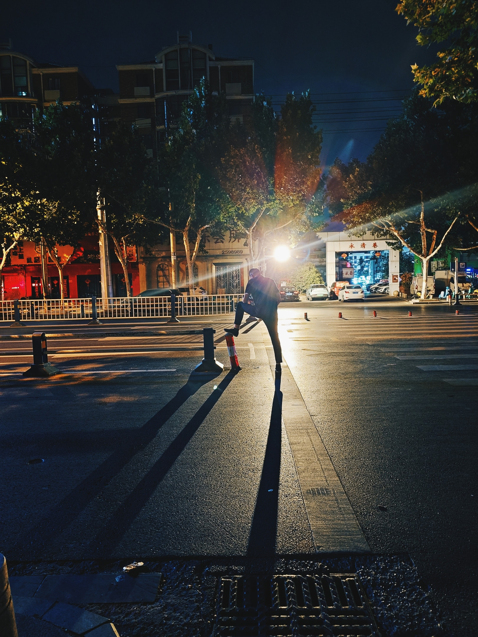 Man resting in street at night, casting shadows from back-lighting.