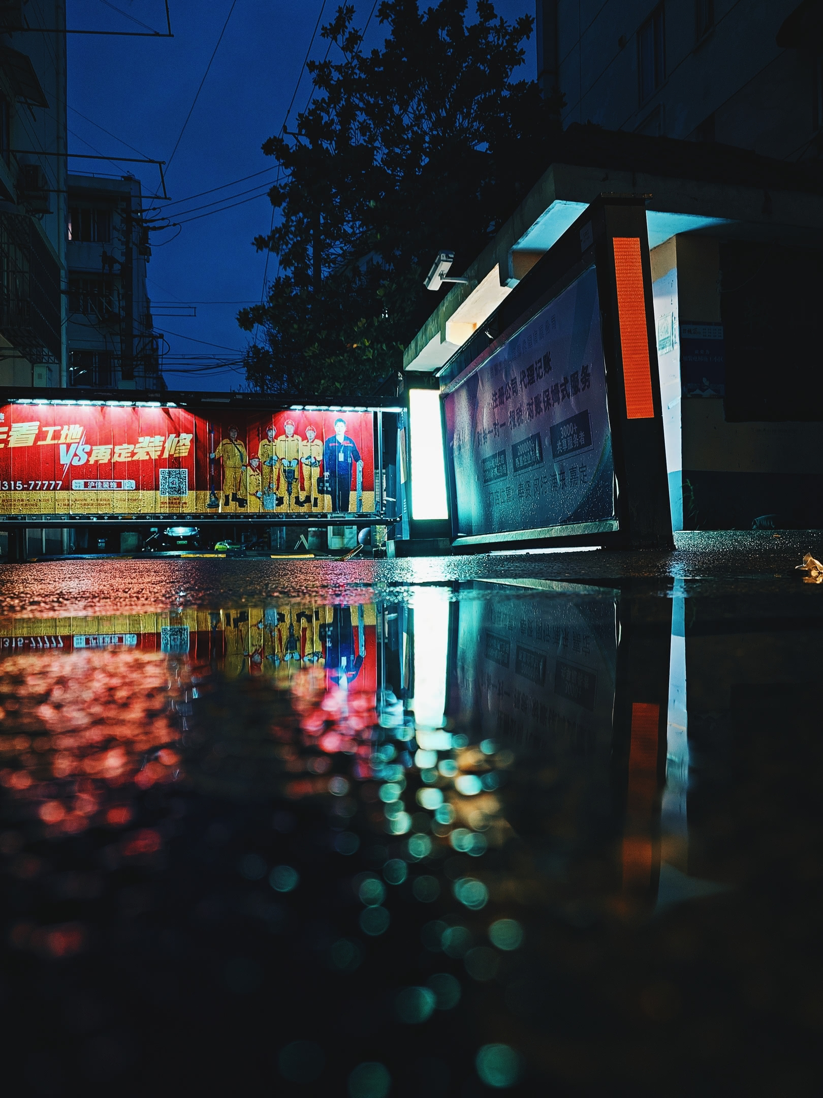 Illuminated apartment complex entrance before dawn. Reflected in a puddle after rain-shower.