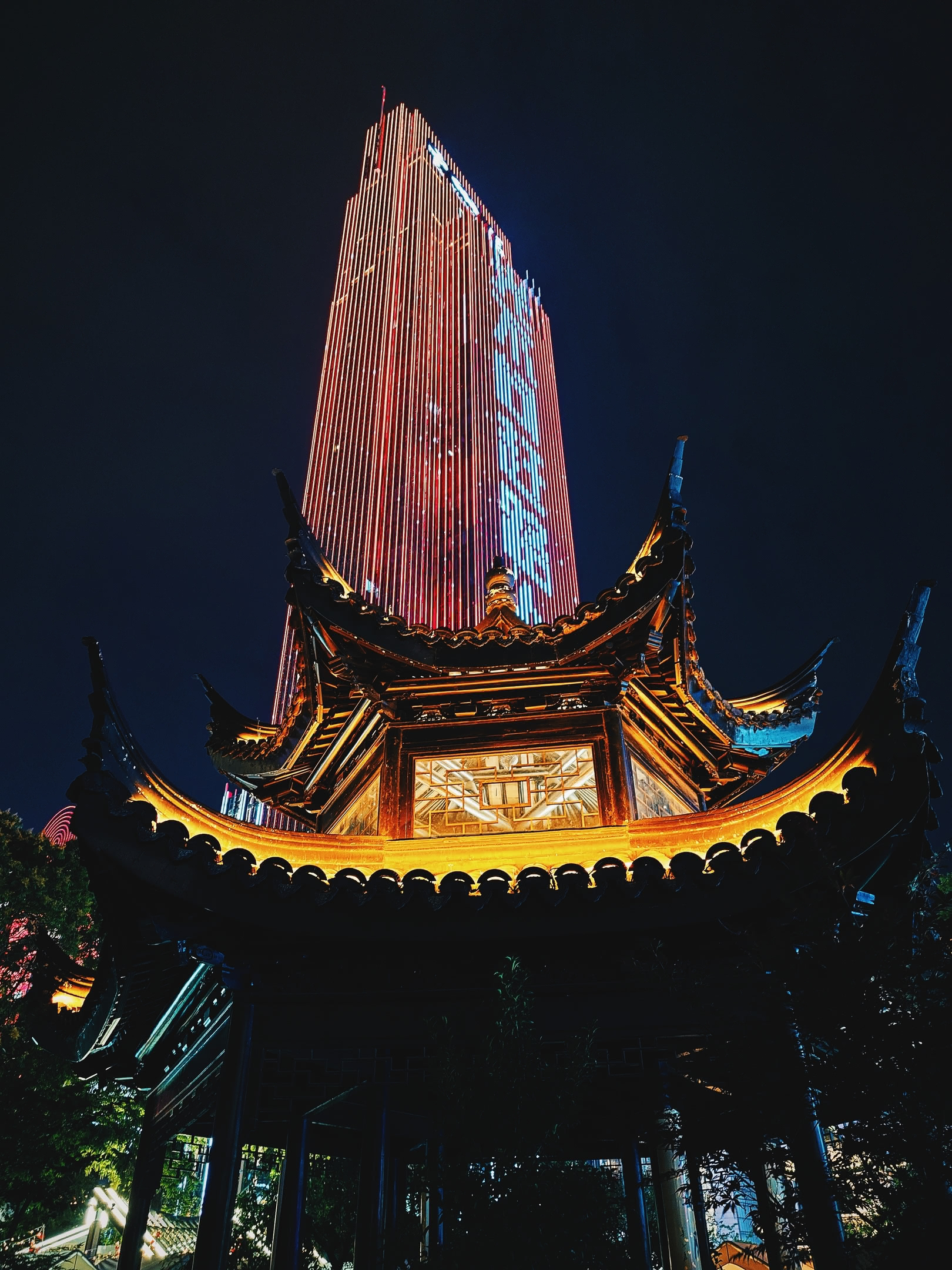 Yunfu Mansion building illuminated with red light at night behind a Chinese pavilion.